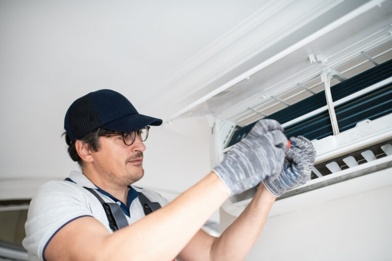 Tech using screwdriver on AC unit ensures HVAC energy efficiency with routine maintenance.