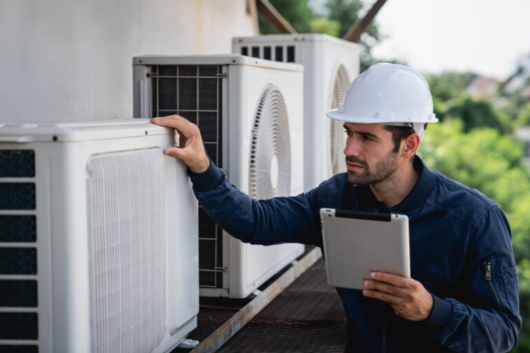 Optimal HVAC Performance: A maintenance worker in a hard hat inspects an outdoor air conditioning unit while holding a tablet.